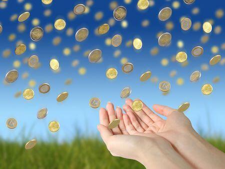 Geldmünzen fallen vom Himmel auf ausgestreckte Hände