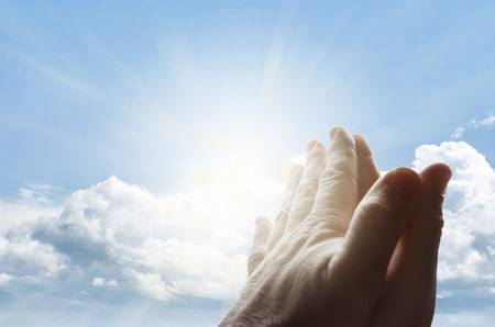 hands together praying in bright sky
